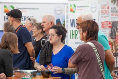 Eine Gruppe von Menschen, darunter junge und ältere Personen, steht bei einer Veranstaltung in einem Saal für eine Pressemitteilung beieinander; einige halten Gegenstände in den Händen. Im Hintergrund sind Informationsplakate und Banner zu sehen.
